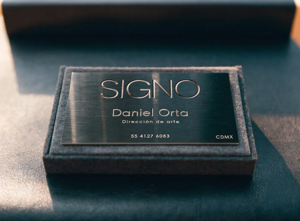 una tarjeta de la marca ficticia SIGNO en metal cepillado con el nombre grabado en hueco, dentro de un estuche de fieltro