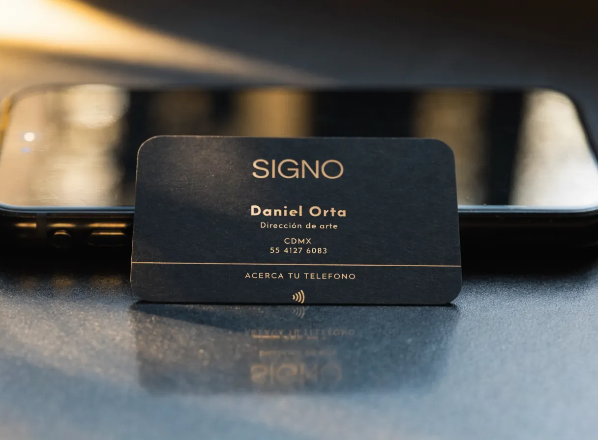 tarjeta de presentación negra con tipografía dorada y un chip NFC, apoyada sobre un teléfono que la lee sin contacto, con la marca ficticia Signo, Daniel Orta, Dirección de arte, CDMX