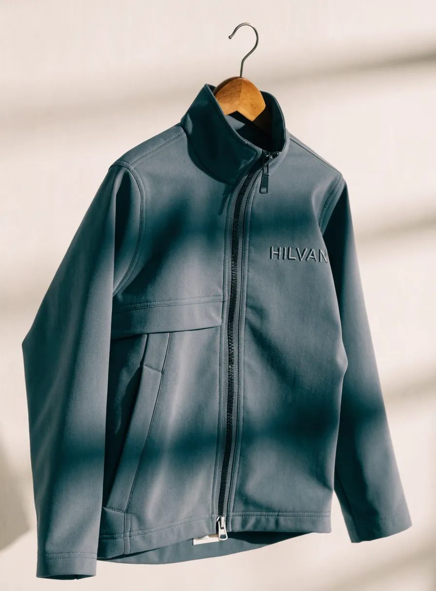 chamarra softshell azul pizarra en un gancho de madera, con cierre completo y la marca HILVAN bordada tono sobre tono en el pecho