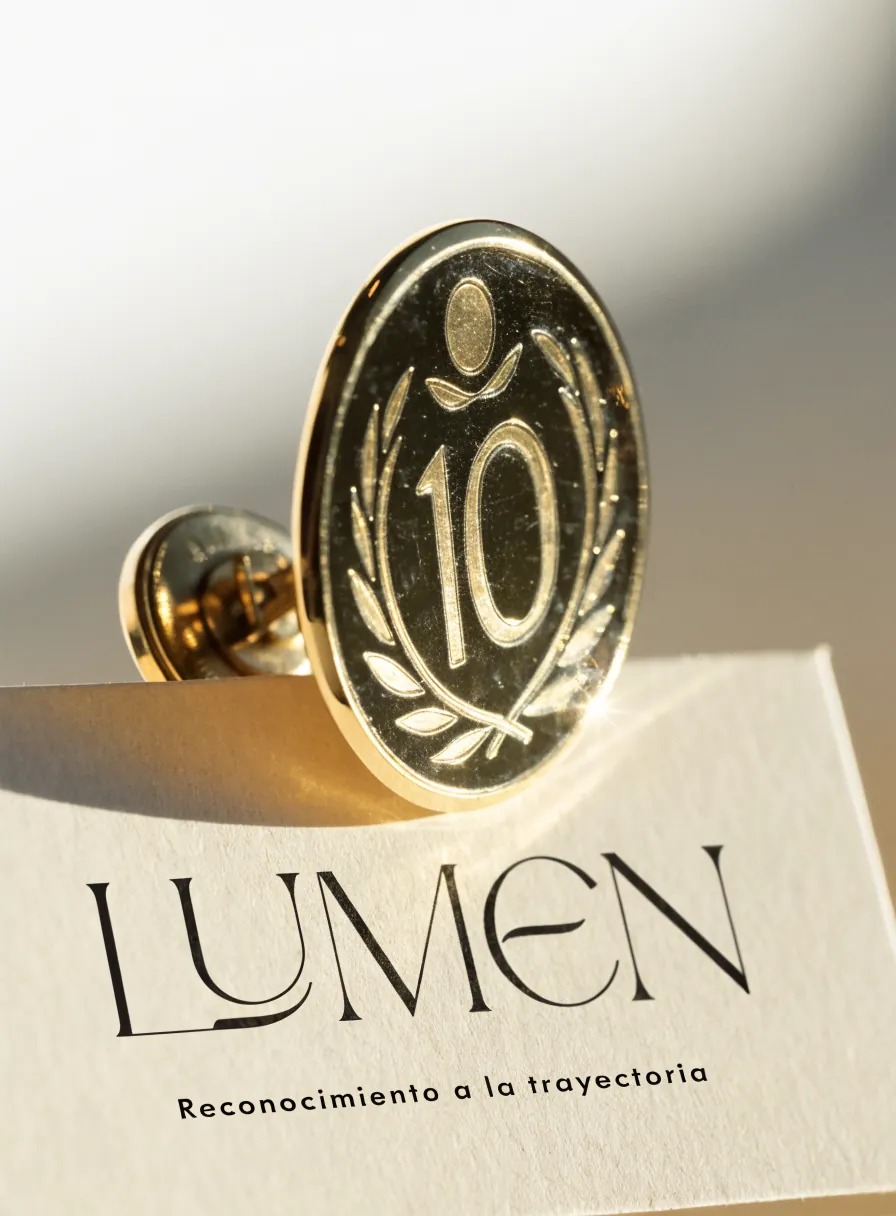 medallón dorado grabado con un número en corona de laurel, prendido sobre una tarjeta LUMEN de reconocimiento a la trayectoria