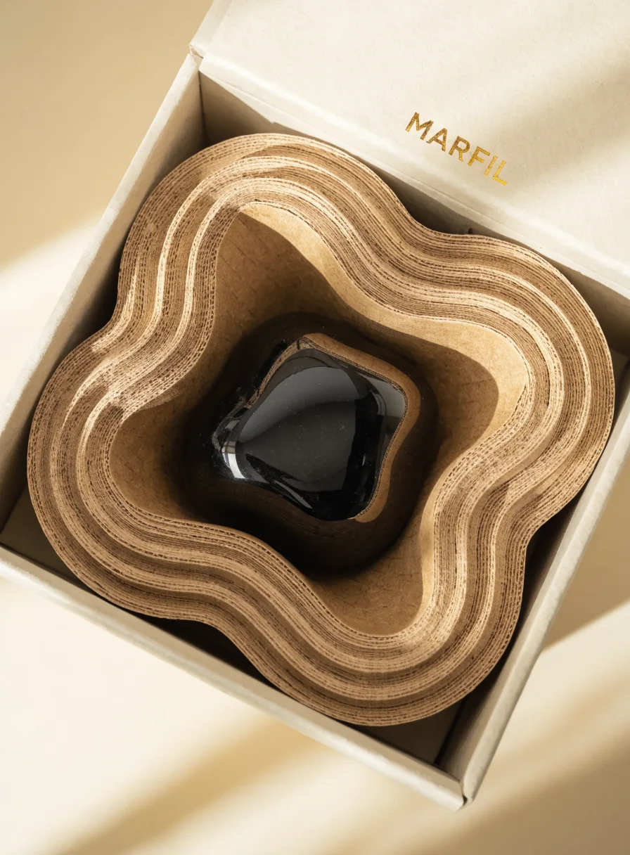 inserto interior en capas de cartón kraft troquelado en forma de nido ondulado que sostiene una pieza en el centro, dentro de una caja marfil con la marca MARFIL en foil oro
