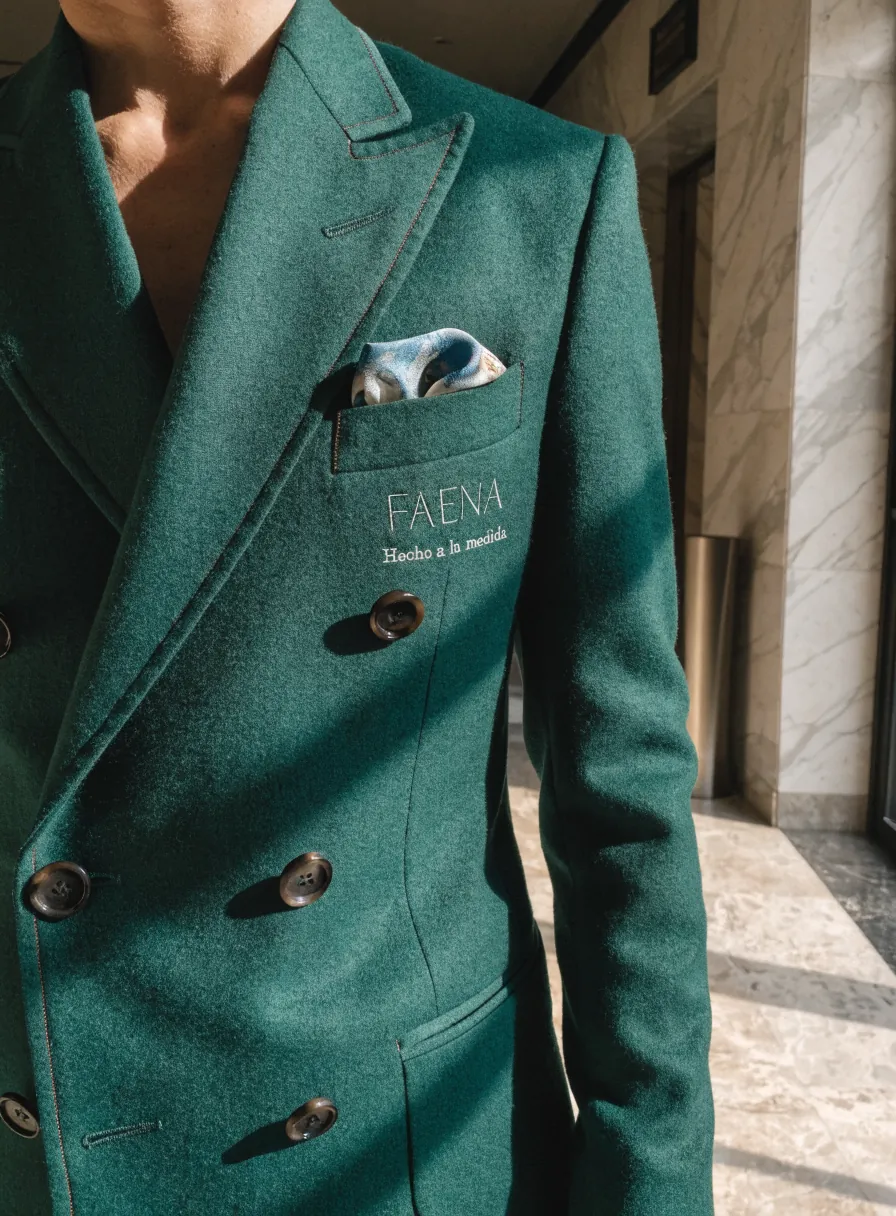saco cruzado de lana verde hecho a la medida, con pañuelo al bolsillo y la marca FAENA con Hecho a la medida bordados en el pecho