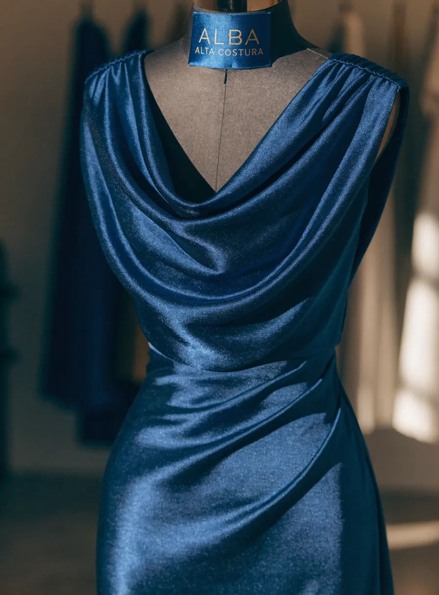 vestido de noche de raso azul profundo sobre un maniquí, con escote drapeado y hombros fruncidos, etiqueta ALBA Alta Costura
