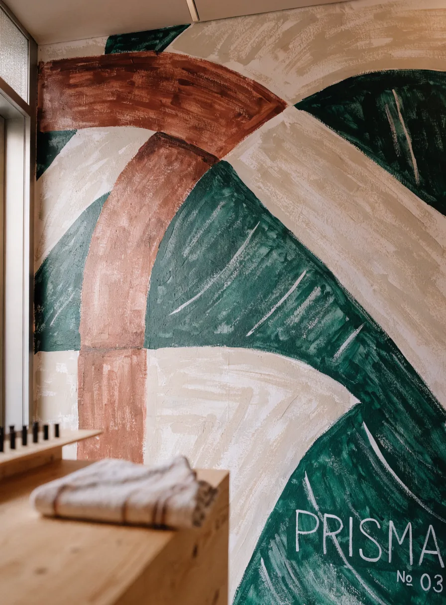 mural pintado a mano con arcos en verde, terracota y crema, firmado y numerado, junto a una banca de madera clara