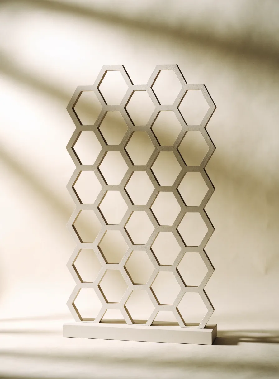 biombo de panal hexagonal lacado en blanco sobre una base delgada, con sombras suaves de hojas cayendo detrás