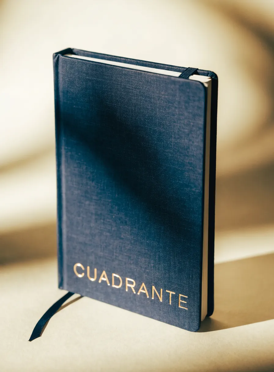 cuaderno de pasta dura forrado en tela azul con la marca en foil de oro, liga y separador de listón