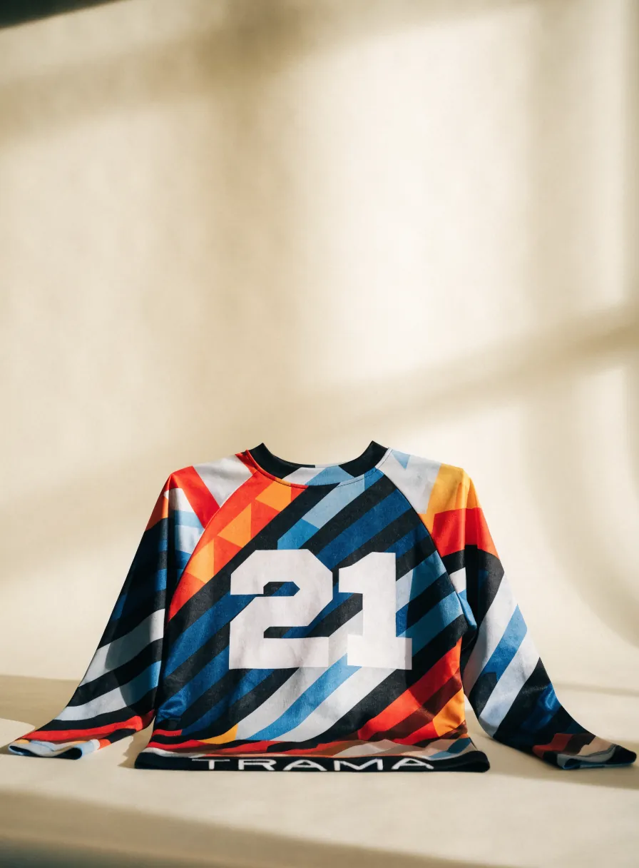 jersey de manga larga con estampado geométrico multicolor sublimado y el nombre TRAMA en la pretina, sobre un fondo crema