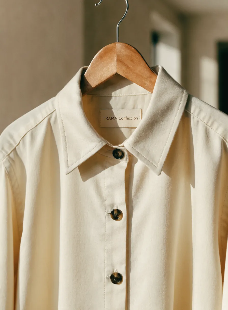 camisa overshirt de sarga color crema en un gancho de madera, con botones de asta y la etiqueta tejida TRAMA Confección en el cuello