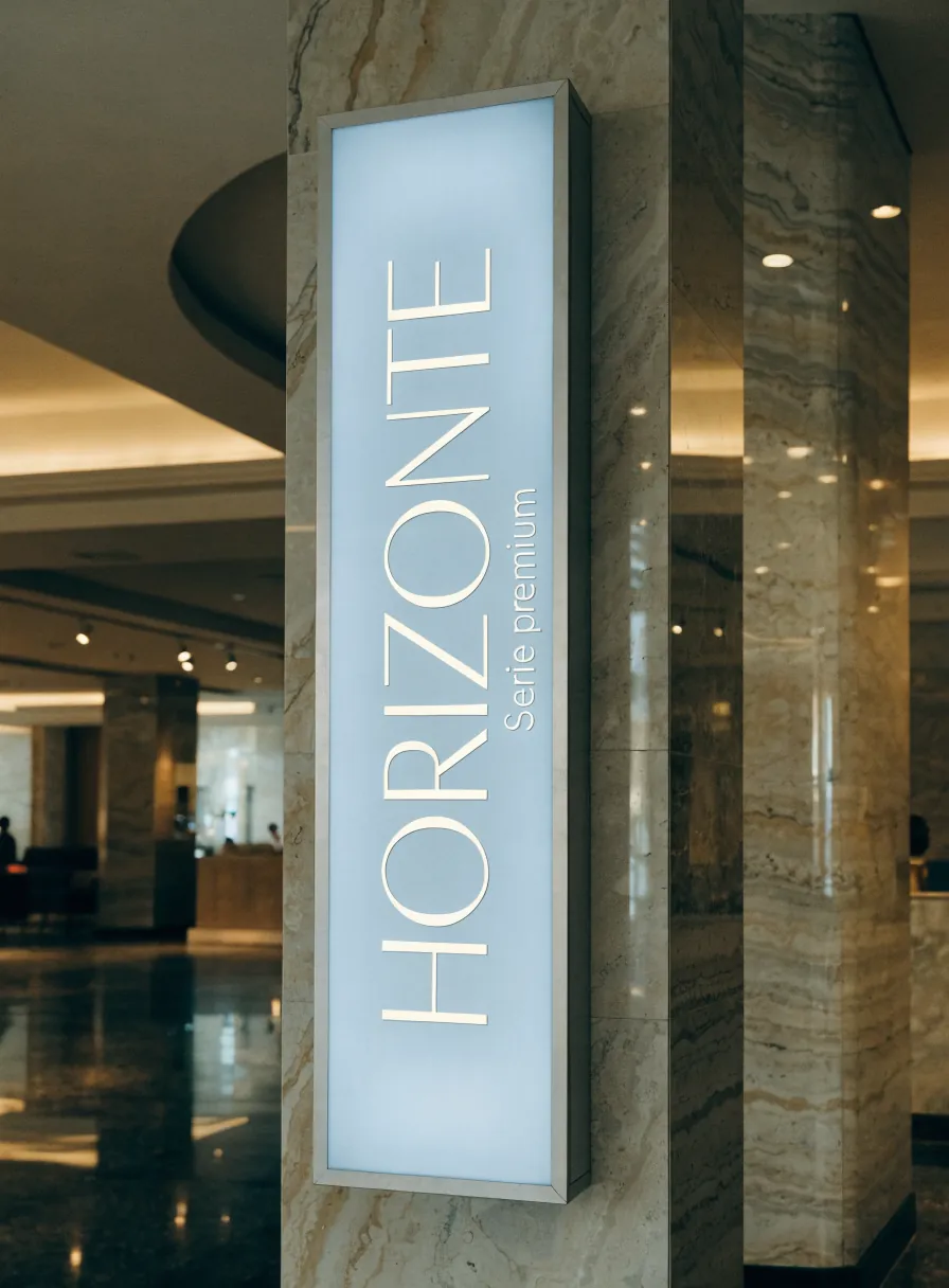 letrero retroiluminado vertical con la marca Horizonte serie premium, en un marco de aluminio sobre una columna de mármol en el lobby de un hotel