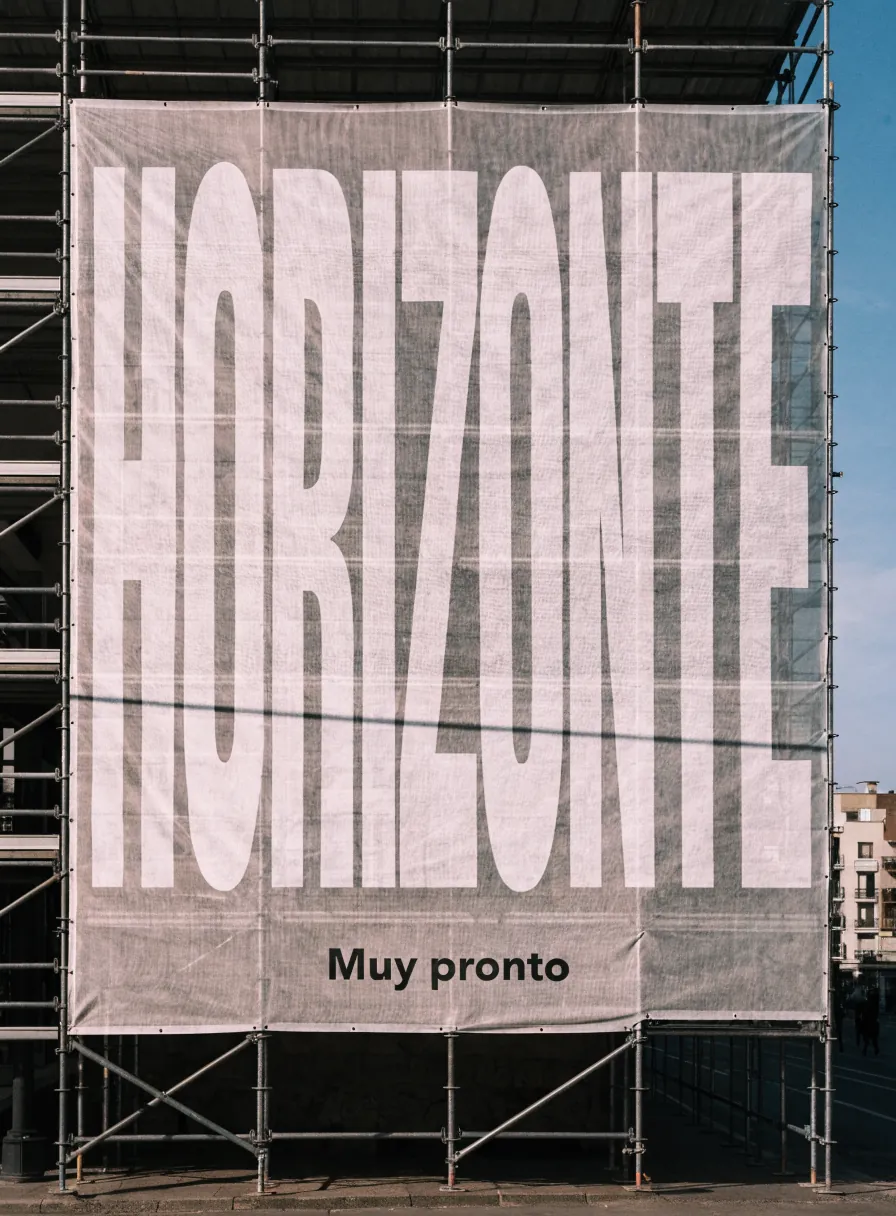 malla de gran formato con la marca Horizonte muy pronto cubriendo un edificio en andamios, con el cielo azul detrás