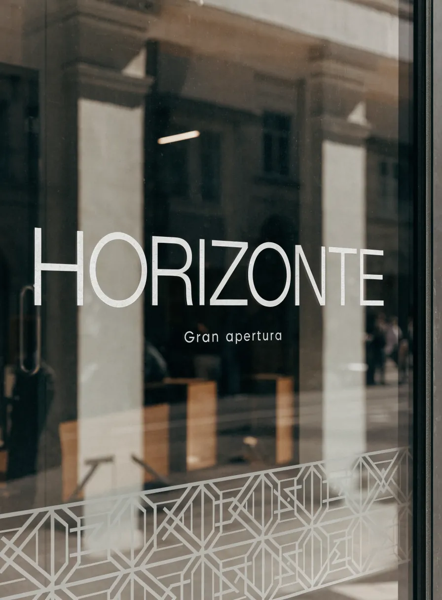 letras Horizonte gran apertura en vinil claro aplicadas sobre el cristal de un local, con la calle reflejada