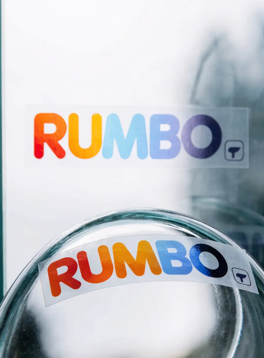 stickers de vinil transparente con la marca Rumbo en degradado de color, pegados sobre vidrio con base de tinta blanca