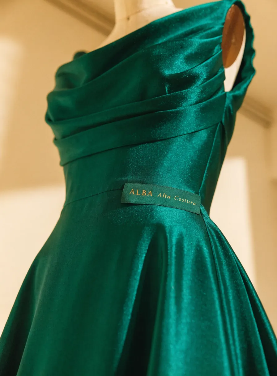 vestido de noche esmeralda de alta costura en un maniquí de sastre, con drapeado a la medida y la etiqueta ALBA Alta Costura en el interior