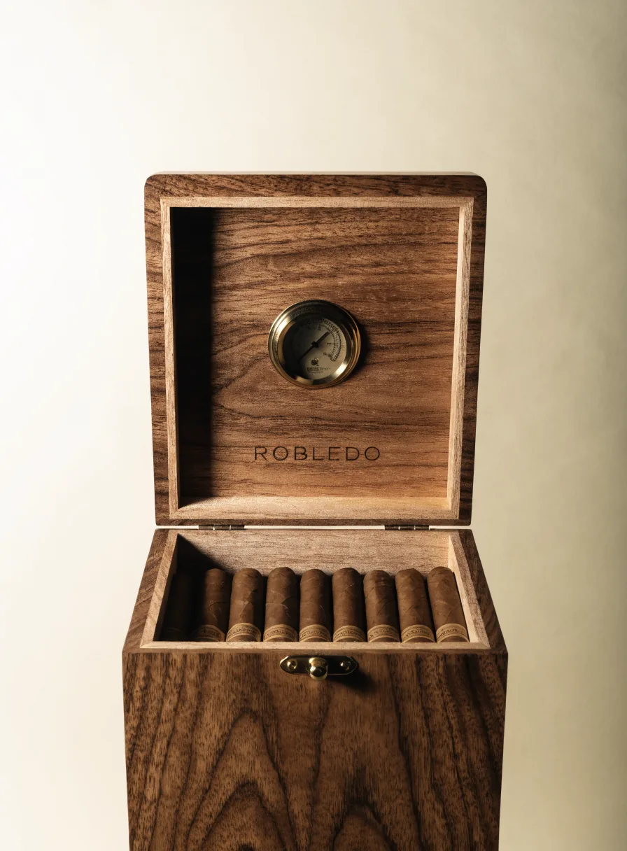 humidor de nogal macizo abierto, con higrómetro de latón en la tapa y la marca ficticia Robledo grabada debajo, con puros dentro