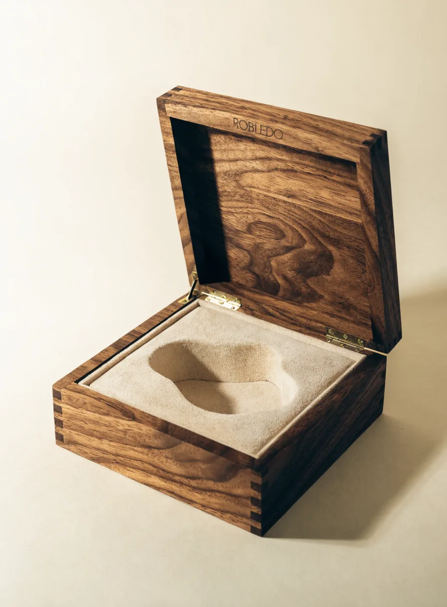 estuche de nogal macizo abierto, con bisagras de latón, interior de gamuza beige troquelado y la marca ROBLEDO grabada en la tapa