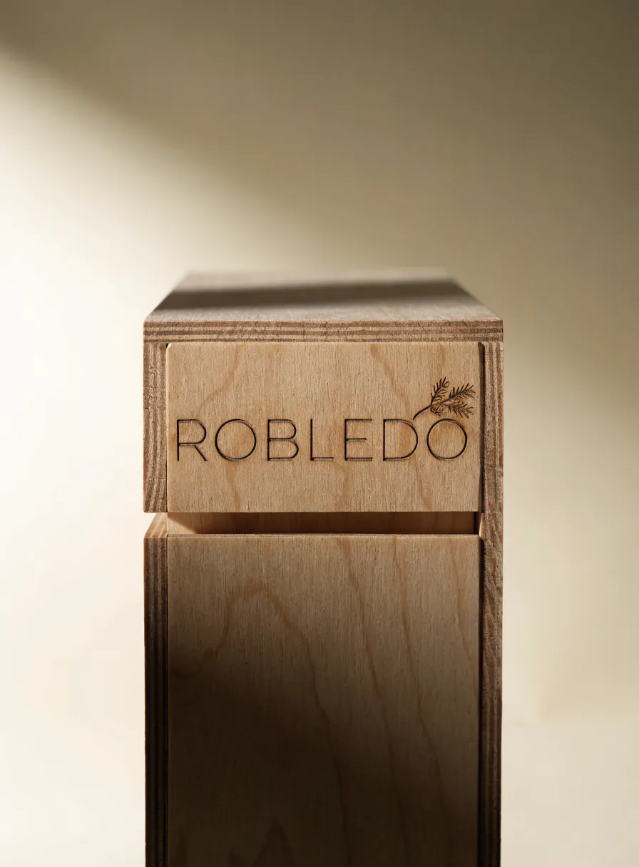 caja de contrachapado claro con tapa corrediza, grabada a láser con la marca ROBLEDO y una ramita de pino