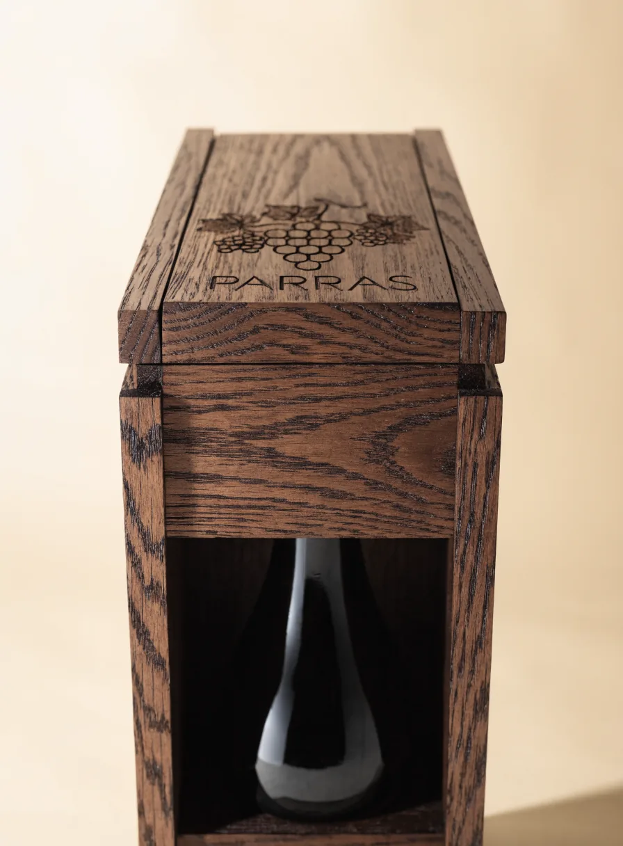 caja de vino de roble con tapa corrediza y racimo de uvas grabado, con la botella visible por una ventana