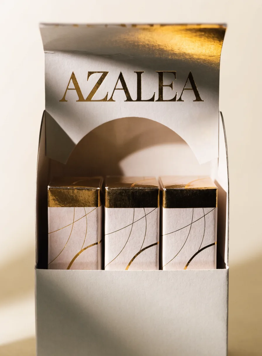 caja de mostrador de la marca Azalea, abierta y con cabecera en foil oro, que exhibe tres estuches con remate dorado