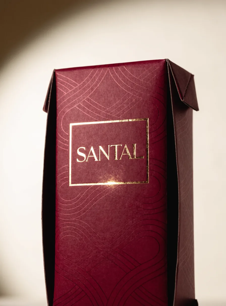 estuche plegadizo tuck-end en cartulina vino de la marca Santal, con un patrón de líneas tono sobre tono y el nombre en un marco de foil oro