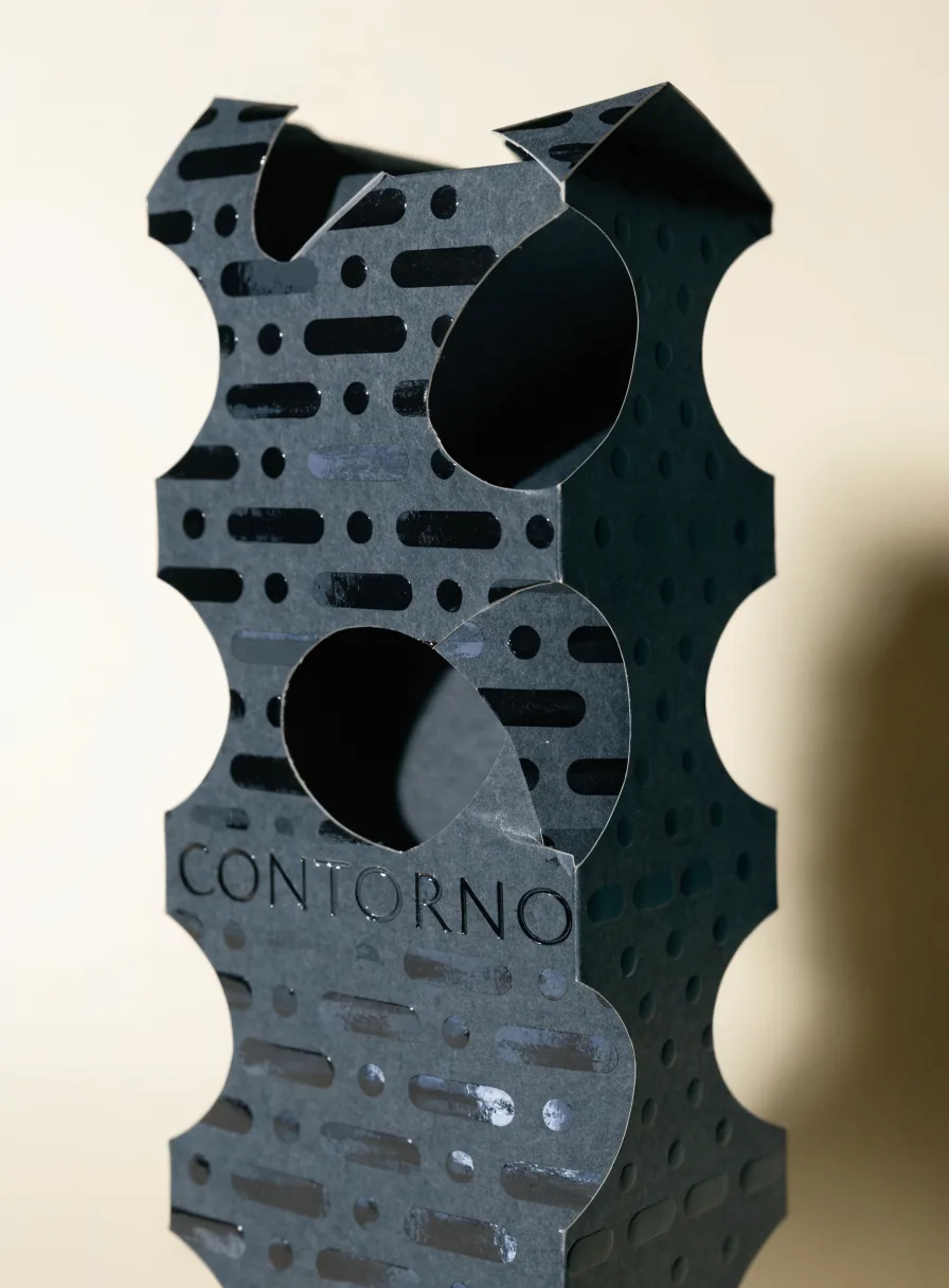 estuche de papel negro troquelado con formas caladas y el nombre de la marca en relieve