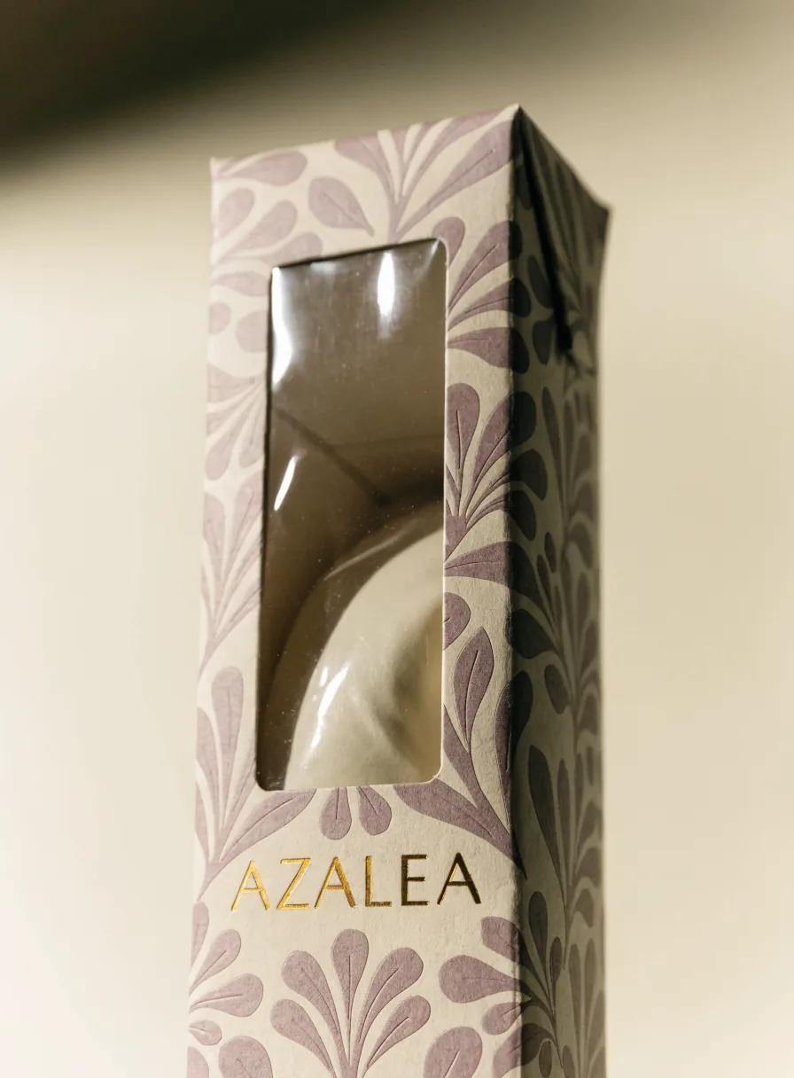 estuche alto con patrón botánico malva de la marca Azalea, con una ventana troquelada y film que deja ver el producto adentro y el nombre en foil oro