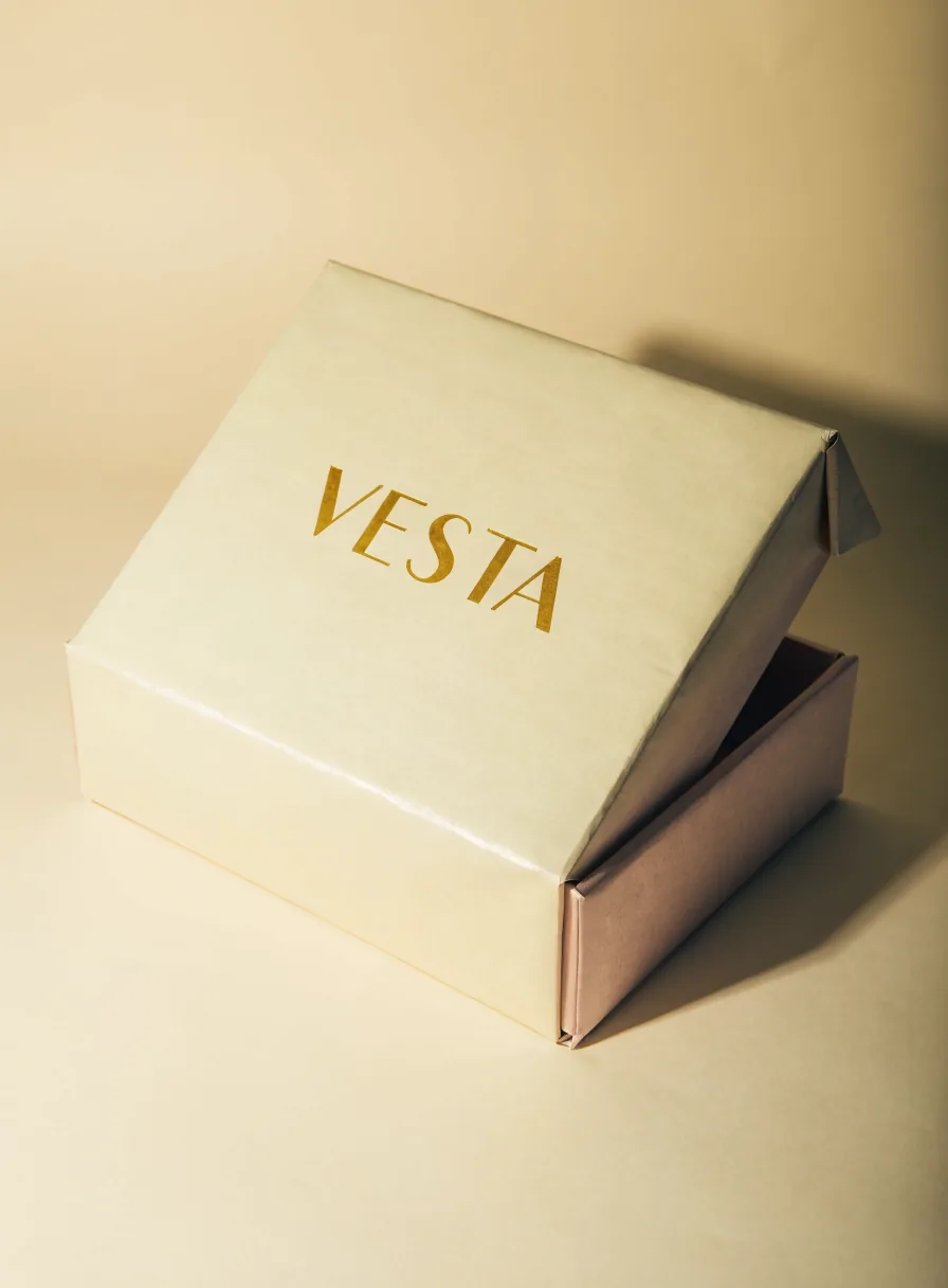 caja rígida forrada color hueso abierta con la palabra Vesta en foil oro y el interior forrado en rosa palo