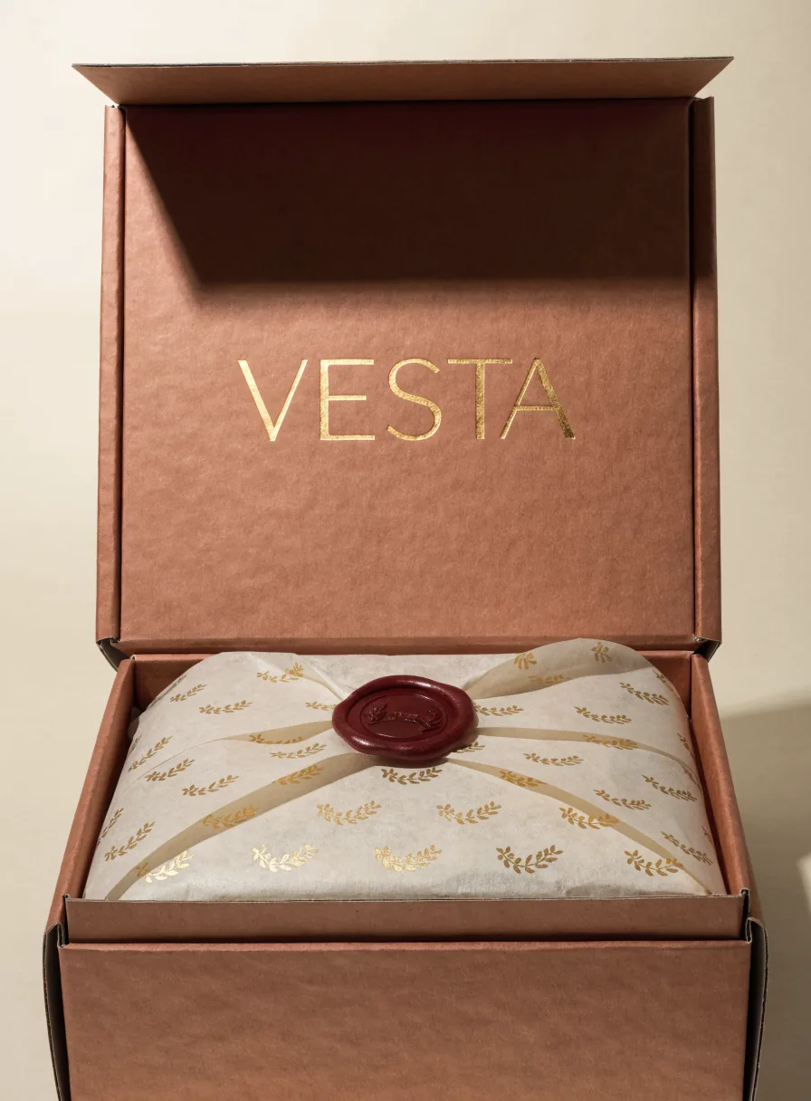 caja mensajera rígida color terracota abierta con la palabra Vesta en foil oro, papel de china con estampado dorado y un sello de lacre vino