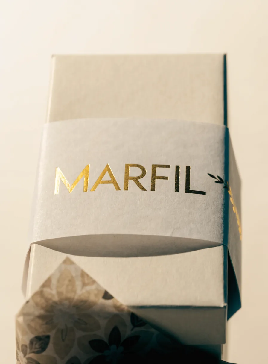 caja marfil cerrada con una fajilla de papel con la marca MARFIL en foil oro y papel china de patrón dorado asomando por la base
