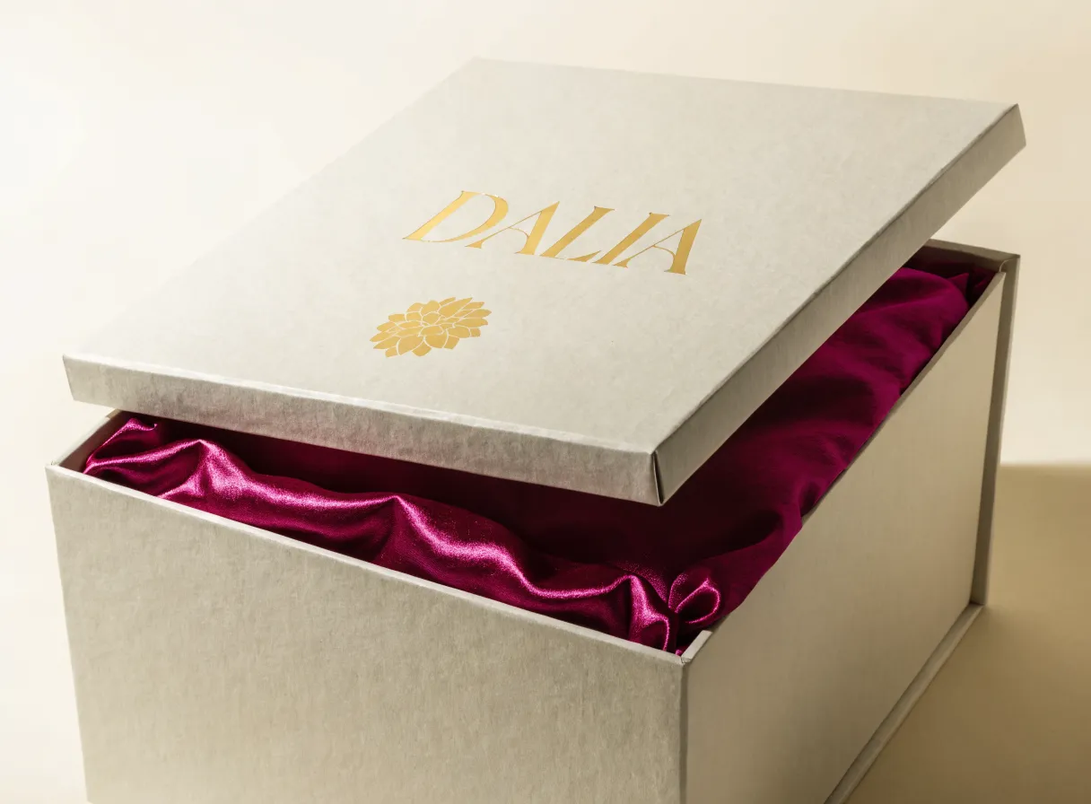 caja rígida gris perla con la palabra DALIA y una flor en foil de oro sobre la tapa, forrada por dentro en satín magenta