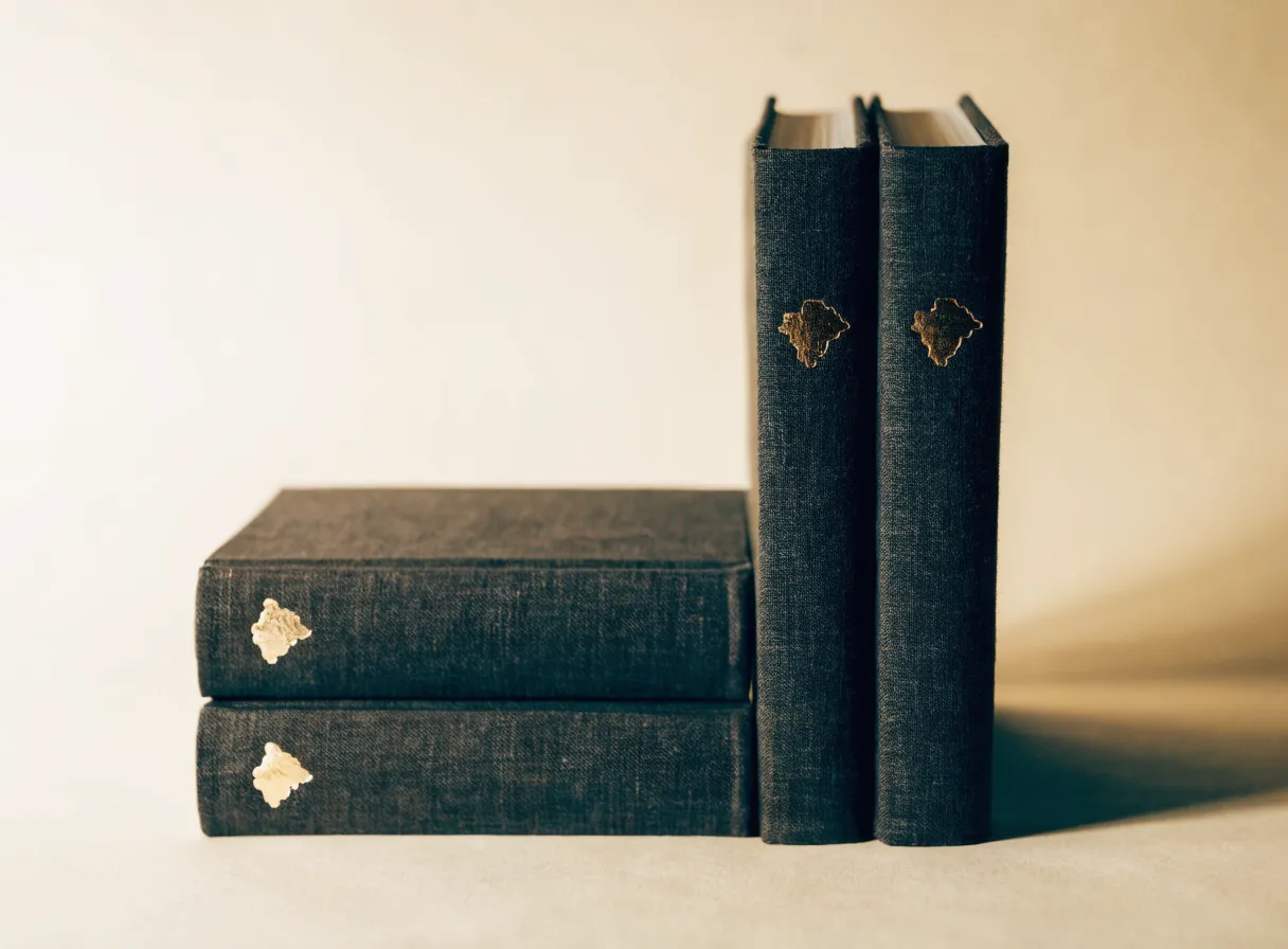 libros entelados en gris carbón con un emblema en foil dorado, apilados y de pie