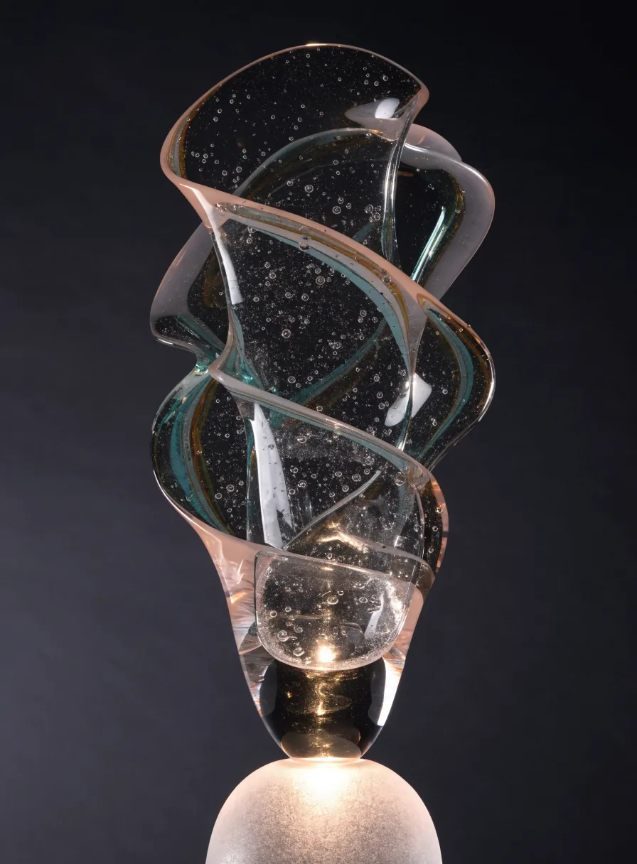 escultura de cristal soplado en espiral con burbujas internas y detalles en verde y cobre, iluminada desde la base
