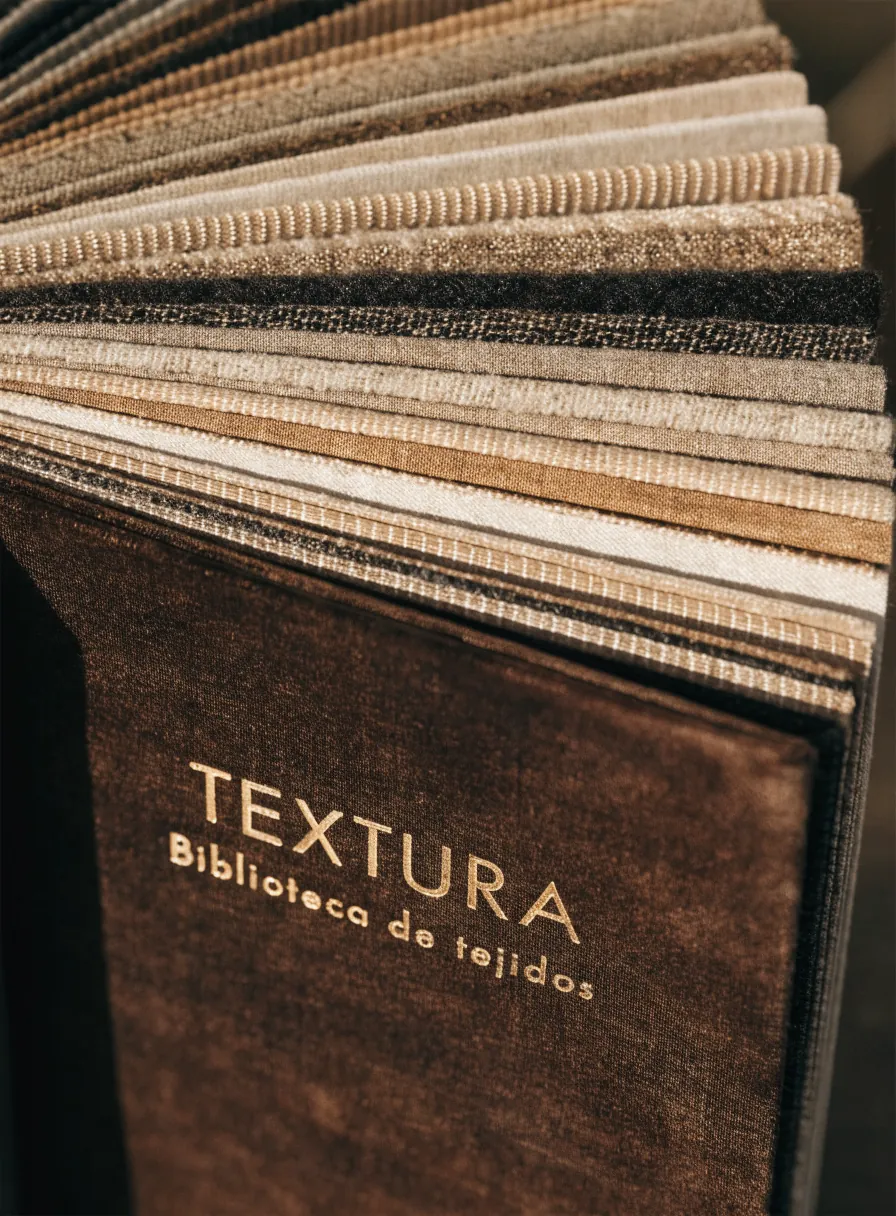 muestrario de tejidos abierto en abanico con decenas de telas en tonos graduados y la marca TEXTURA estampada en dorado en la pasta