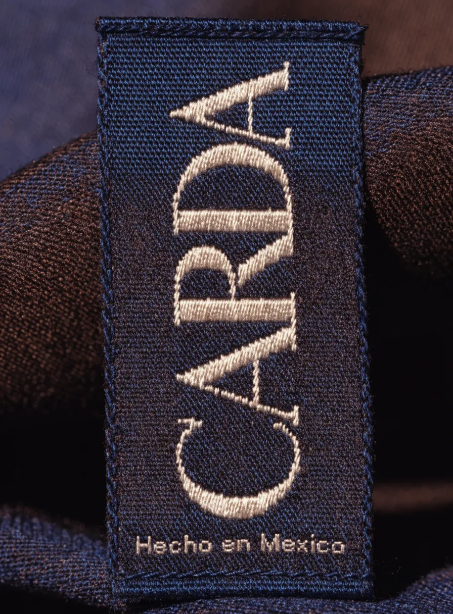 etiqueta tejida en jacquard con la marca CARDA en hilo marfil sobre fondo índigo, cosida a una tela doblada