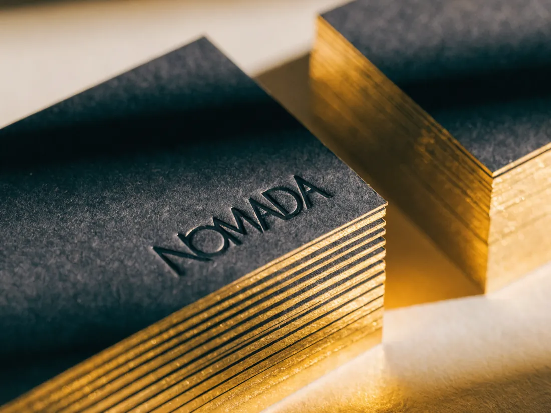 bloque de tarjetas de papel negro con el nombre NOMADA en deboss y el canto dorado brillante en todo el filo