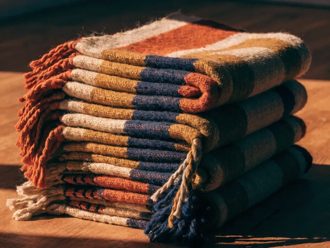 Pila de textiles tejidos a mano con flecos en franjas terracota, azul y mostaza