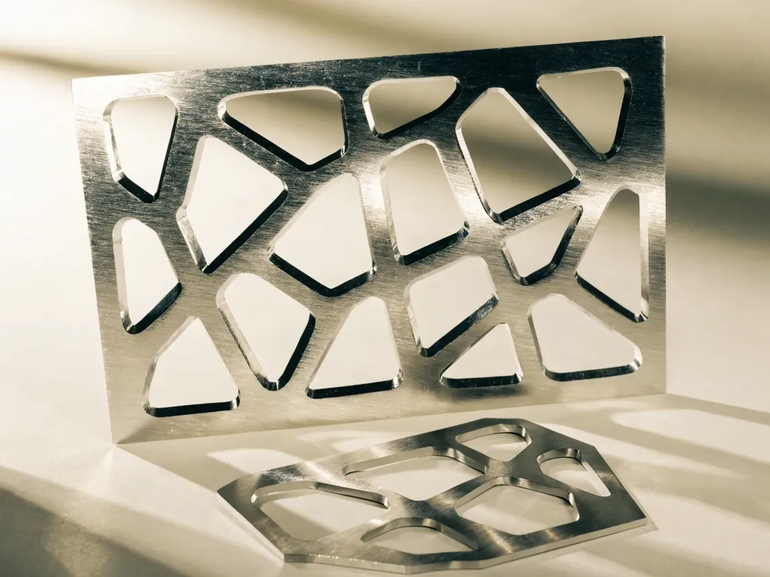 panel de metal cepillado con un patrón orgánico de celdas calado a láser, de pie e iluminado de lado, con su recorte junto a la base