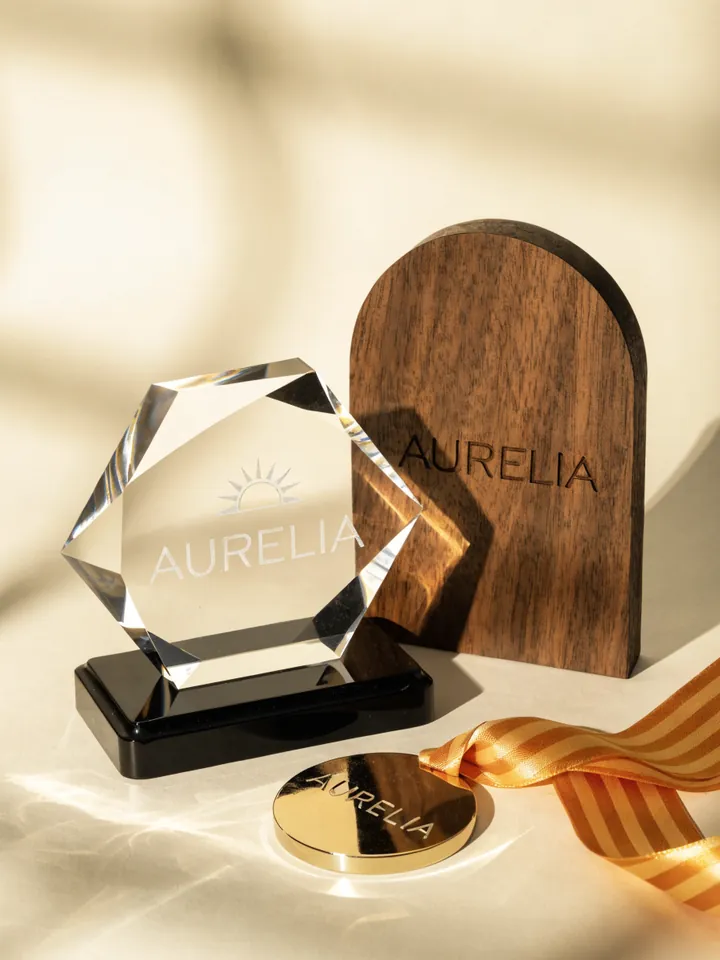 juego de trofeo de cristal, placa y medalla con la misma marca grabada, alineados sobre una superficie oscura