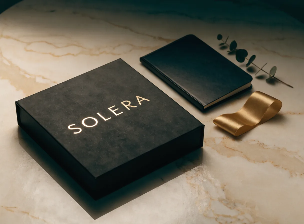 caja rígida negra de regalo de fin de año con la marca Solera en foil dorado, junto a una libreta de piel negra sobre una mesa de mármol