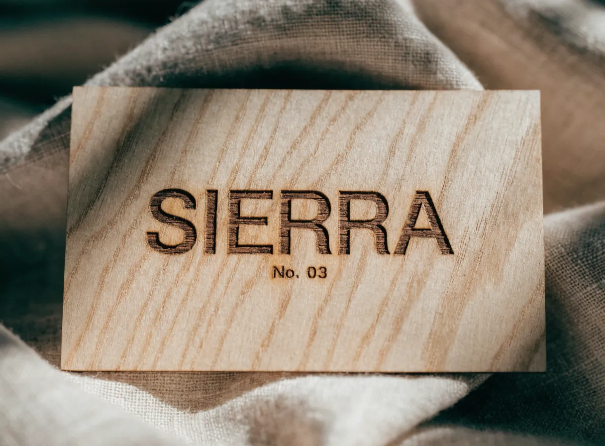 tarjeta de presentación de madera clara con la veta a la vista, la marca Sierra y el número 03 grabados a láser, sobre una tela de lino