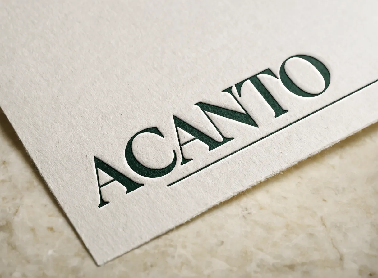 hoja de papel de algodón color crudo sobre mármol beige, con la palabra ACANTO impresa en letterpress verde profundo y hundida en la fibra, y un filete fino corriendo debajo