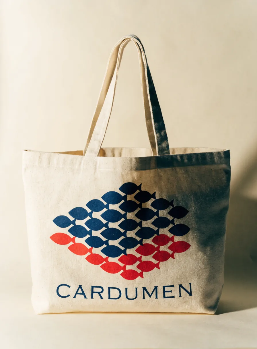 tote grande de mercado en algodón natural con el mismo cardumen de peces azul marino y rojo serigrafiado y la palabra CARDUMEN debajo