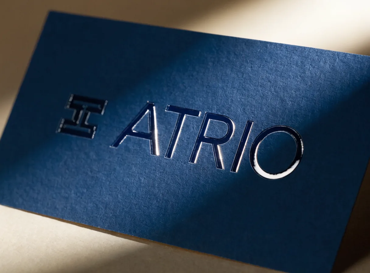 Acercamiento en escorzo de una tarjeta azul marino donde el barniz spot UV de la palabra ATRIO devuelve una banda de luz rasante