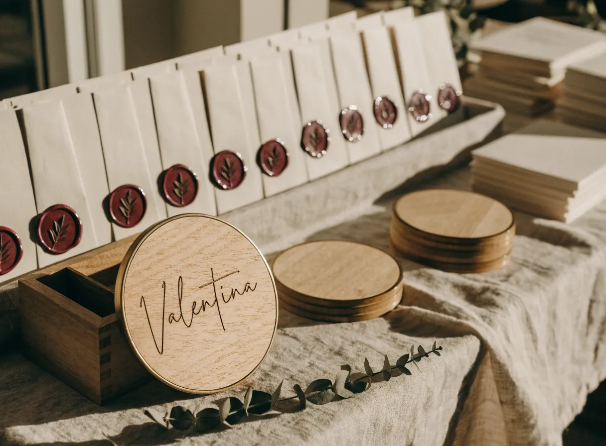 disco de madera grabado con el nombre Valentina al frente sobre lino, y detrás el pedido completo de esa boda, con la fila de sobres cerrados con lacre y las pilas de discos todavía en blanco