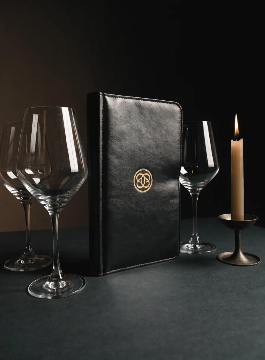 carta de vinos encuadernada en negro con emblema dorado junto a copas y vela