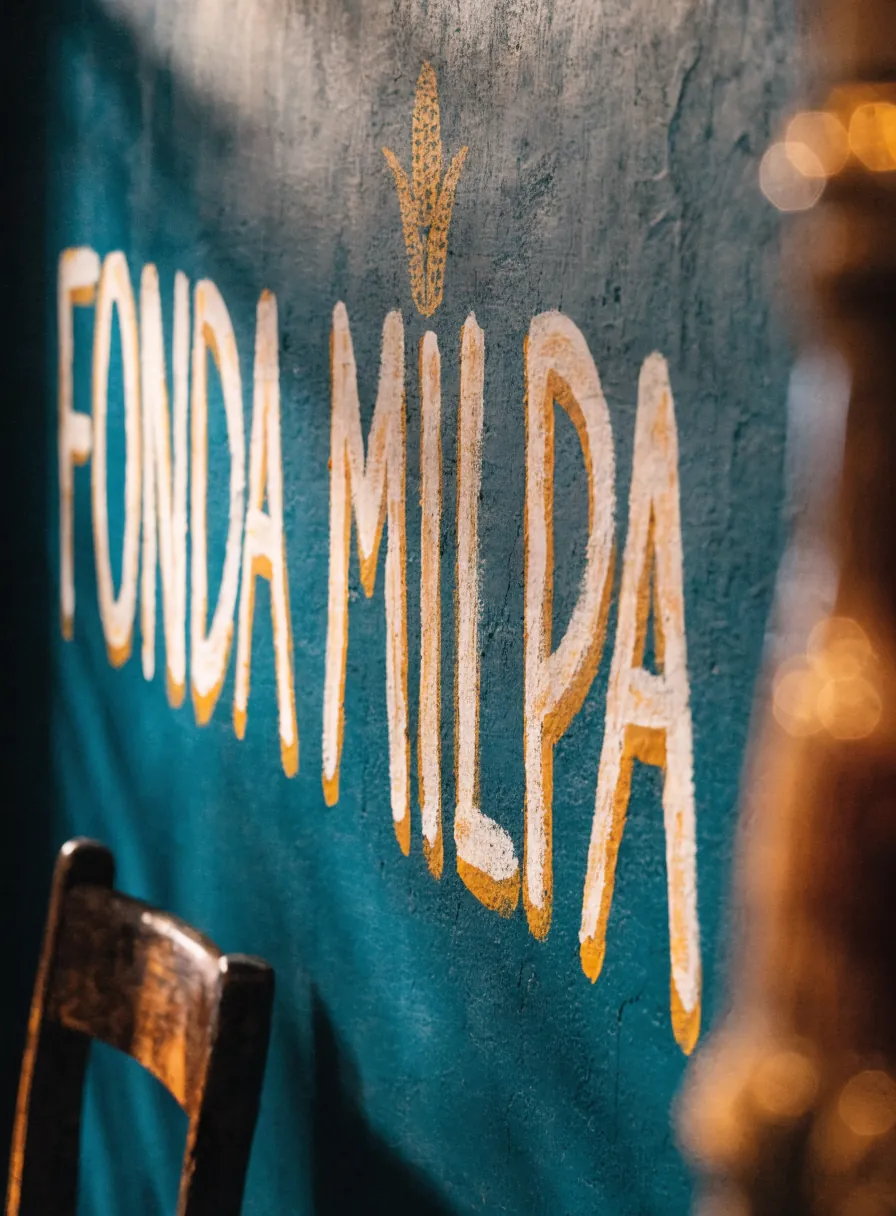 mural pintado a mano sobre pared teal con el nombre Fonda Milpa a brocha en una cantina cálida