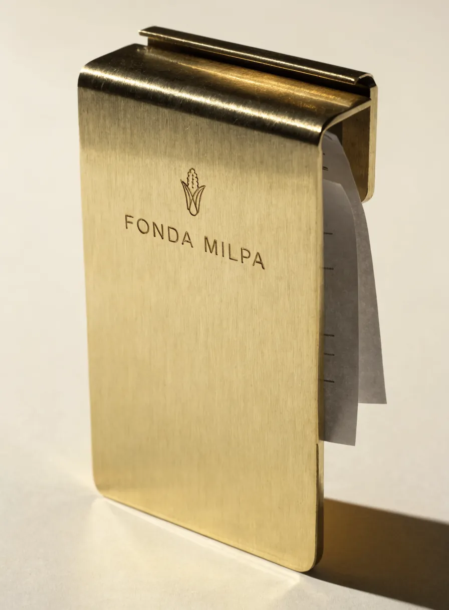 portacuentas plegado de latón cepillado con un emblema y una marca ficticia grabados, sosteniendo una nota de papel