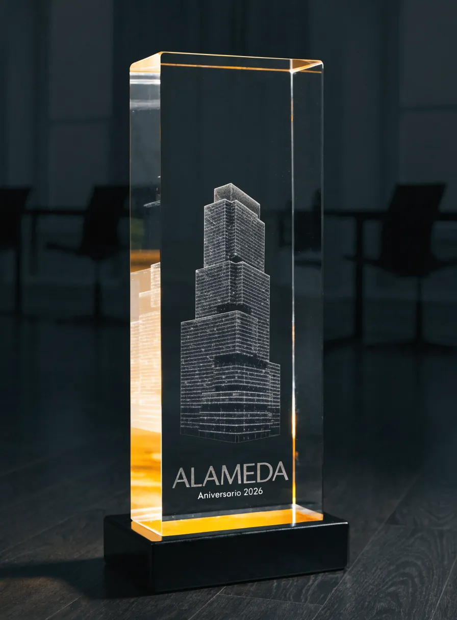 bloque vertical de cristal sobre una base negra encendida, con una torre de oficinas grabada en tercera dimensión dentro, y las palabras Alameda y Aniversario 2026 al pie