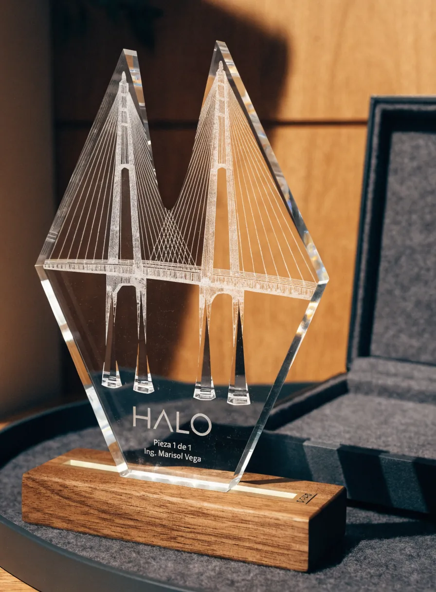 trofeo de cristal cortado en punta con un puente atirantado grabado en tercera dimensión dentro de la masa, sobre una base de nogal encendida por debajo, junto a su estuche forrado en gris