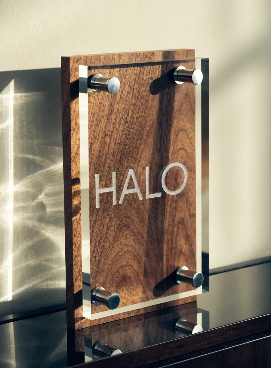 hoja de cristal transparente separada con cuatro tornillos de acero sobre una tabla de nogal, con la palabra Halo arenada por detrás