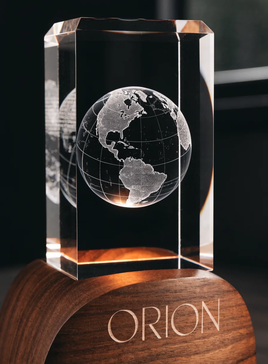 bloque biselado de cristal K9 sobre una base de nogal encendida, con un globo terráqueo grabado en tercera dimensión dentro de la masa y la palabra Orion grabada en la madera de la base
